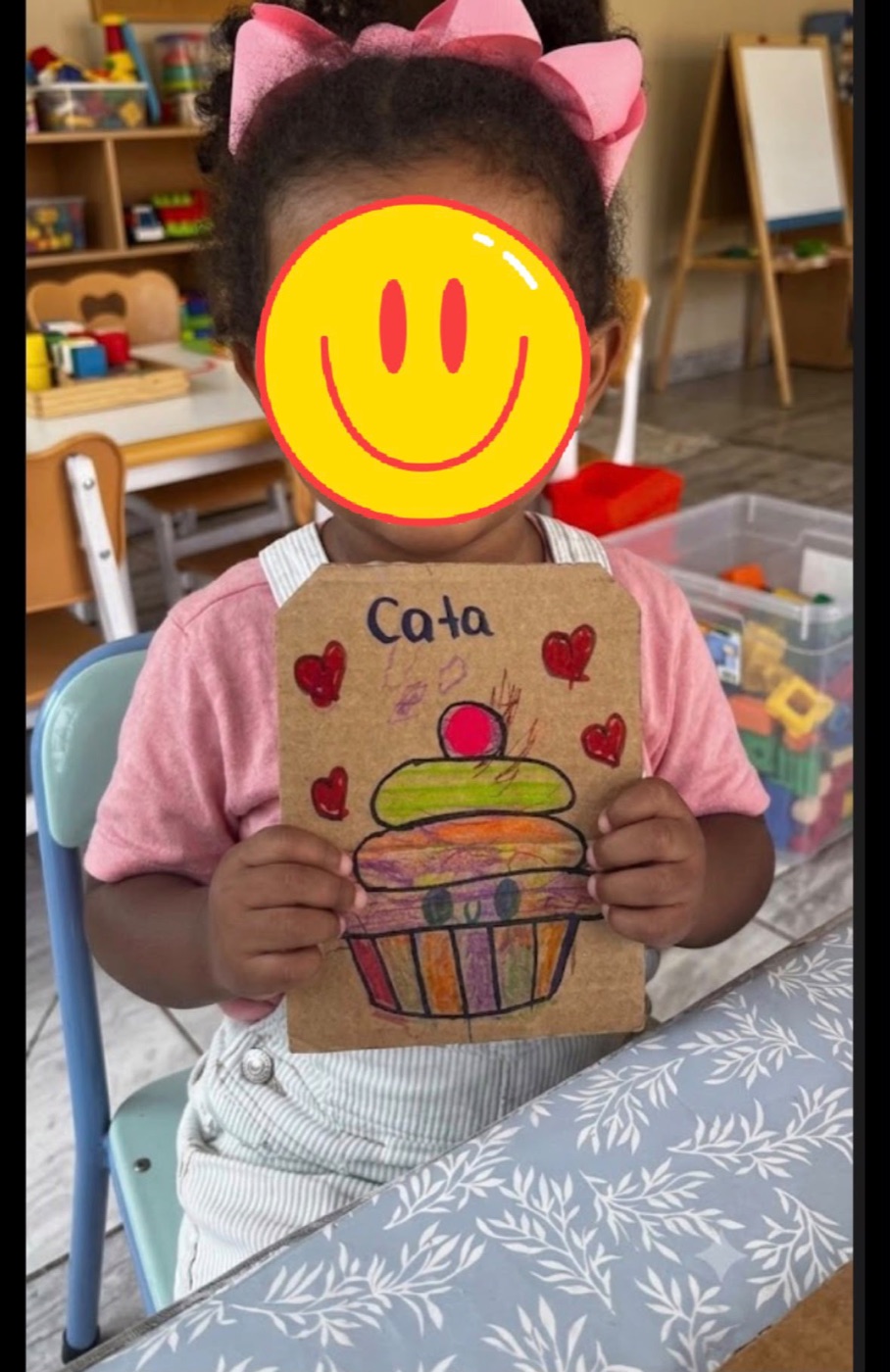 Child holding a colorful art project with face covered for privacy