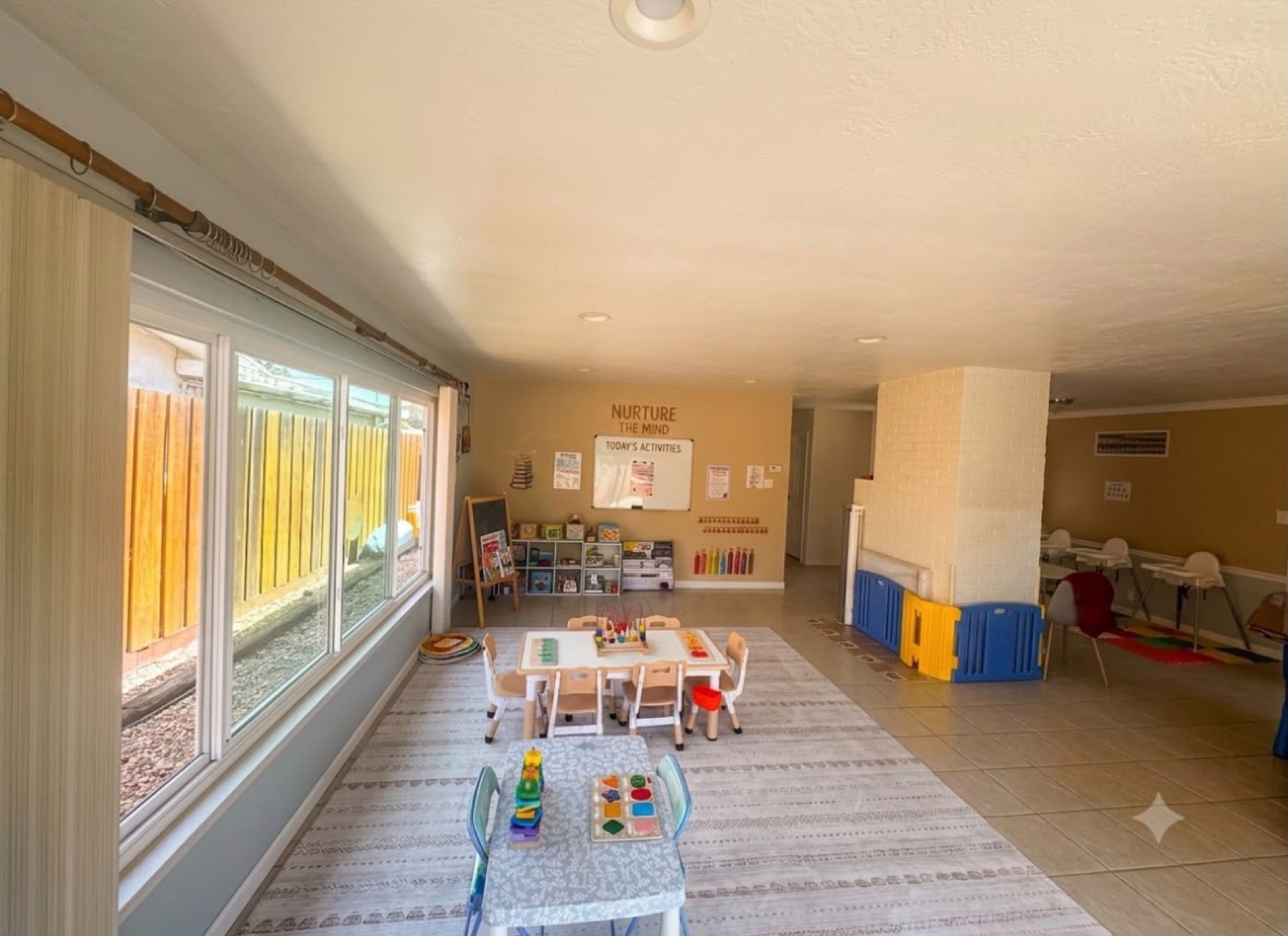 Spacious indoor childcare room with learning tables, toys, and open play areas