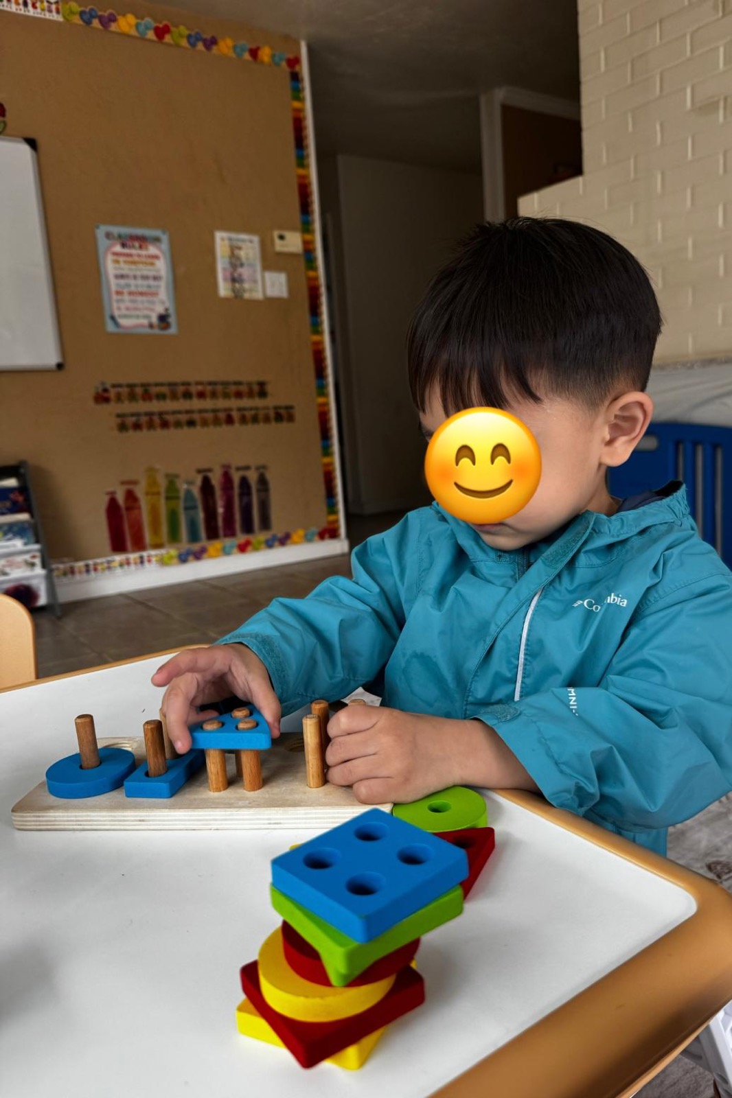 Child practicing fine-motor skills with colorful wooden shape pieces at Ale's Home Childcare with face covered for privacy