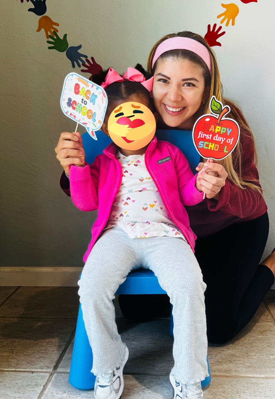 Ale smiling with a child holding first day of school signs with the child face covered for privacy
