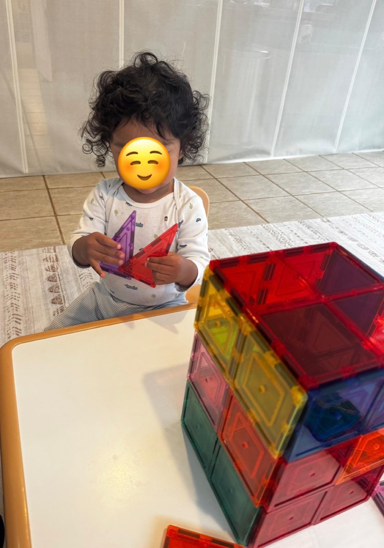 Child building with colorful magnetic tiles at Ale's Home Childcare with face covered for privacy
