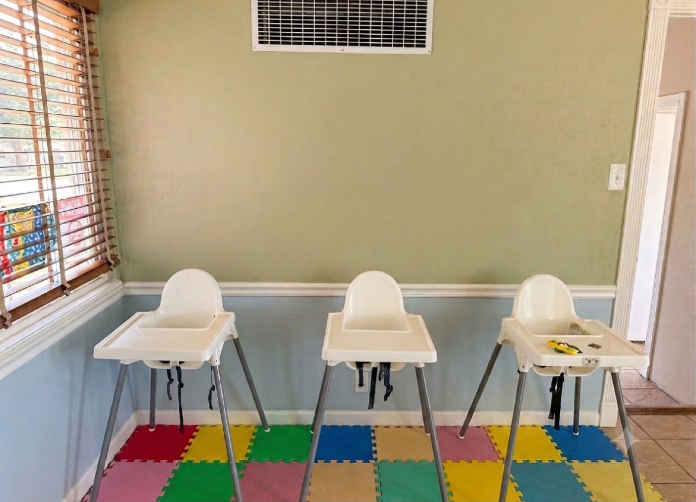 Childcare mealtime area with high chairs on colorful floor mats