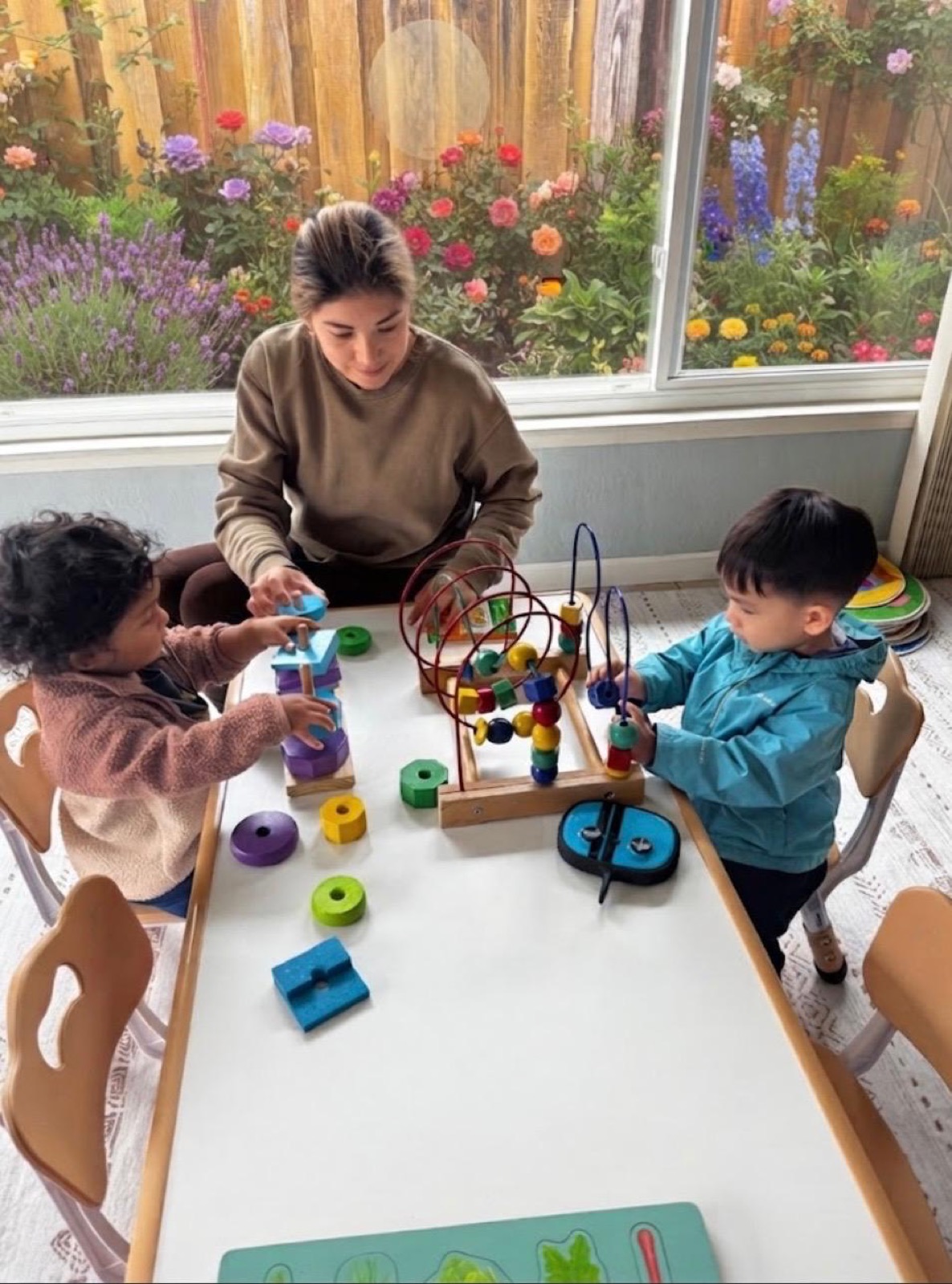 Ale guiding two children through hands-on learning at a child-sized table by the garden window